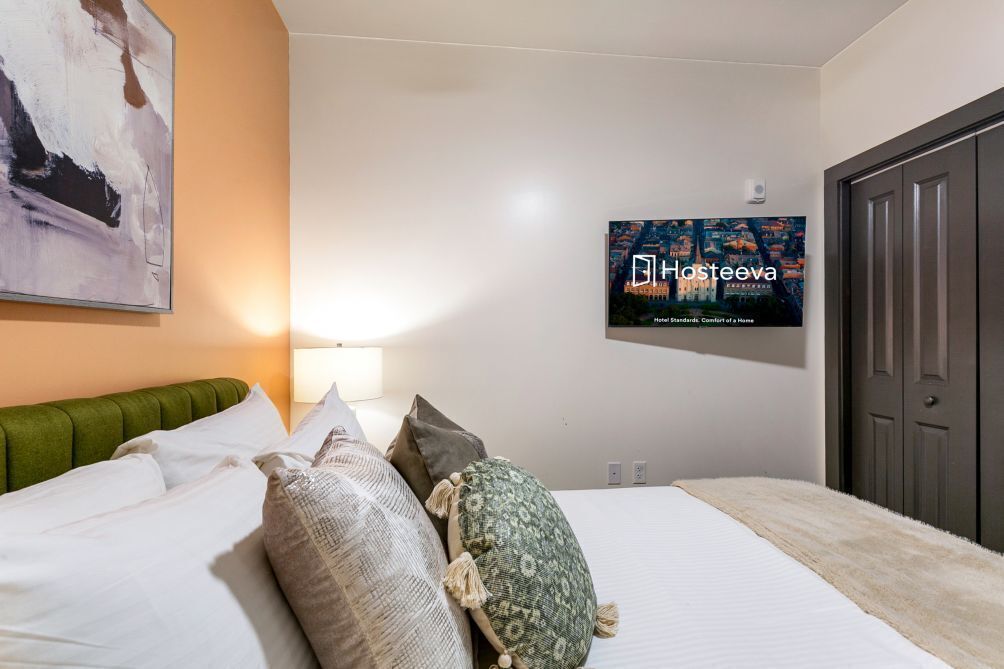 Ein Hotelzimmer mit einem Bett, Kissen, einem an der Wand befestigten Fernseher und einer Tür.