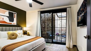 Un dormitorio con cama, ventilador de techo, ventana grande con cortinas y vista al exterior.