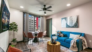 A modern living room with a blue sofa, a round coffee table, and a dining area with chairs and a table.