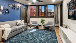 Una sala de estar moderna con un sofá gris, dos sillones, una mesa de centro y un gran ventanal con vistas a la ciudad.