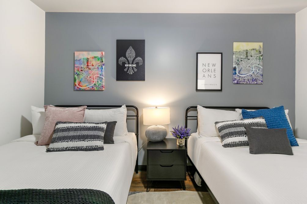 A hotel room with two beds, a nightstand with a lamp, and three framed artworks on the wall.