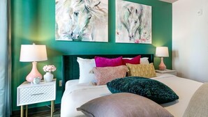 A hotel room with a bed, two bedside tables, a nightstand, and two wall-mounted paintings.