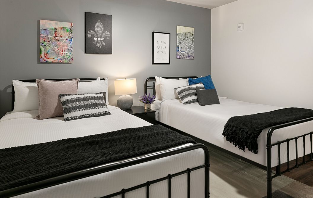 Habitación de hotel con dos camas, una mesita de noche con lámpara y arte mural que representa Nueva Orleans.