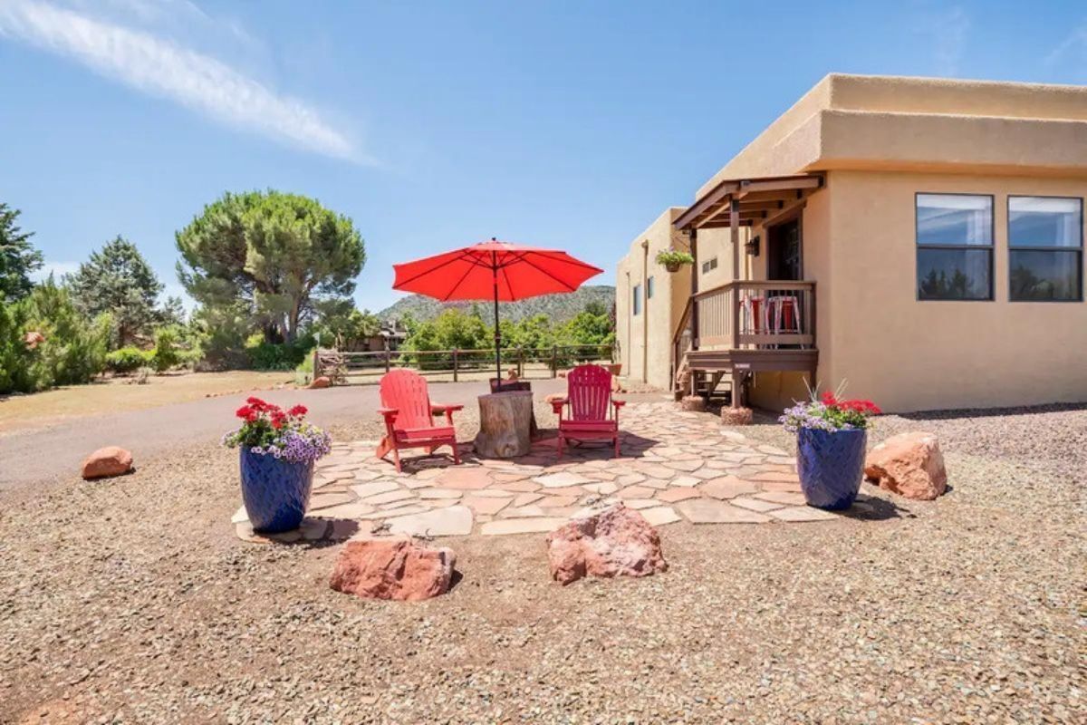A patio with red chairs, a red umbrella, and potted plants.