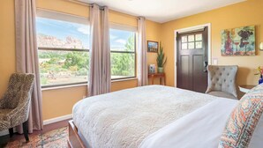 A bedroom with a large bed, a chair, a desk, and a door.