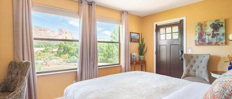 A bedroom with a large bed, a chair, a desk, and a door.