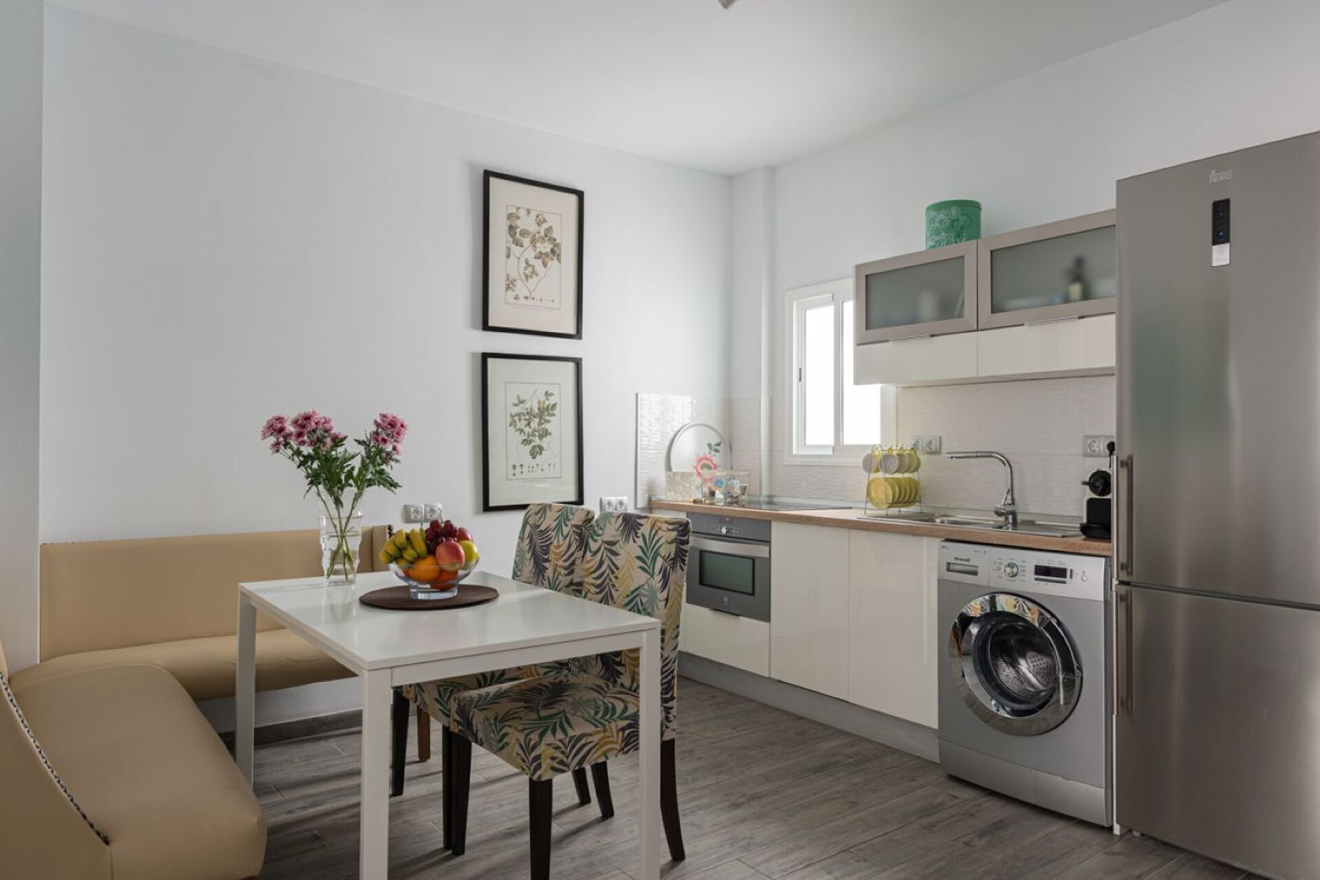 Une cuisine moderne équipée d’un lave-linge intégré, un coin repas avec une table et des chaises, et des œuvres d’art encadrées qui ornent les murs.