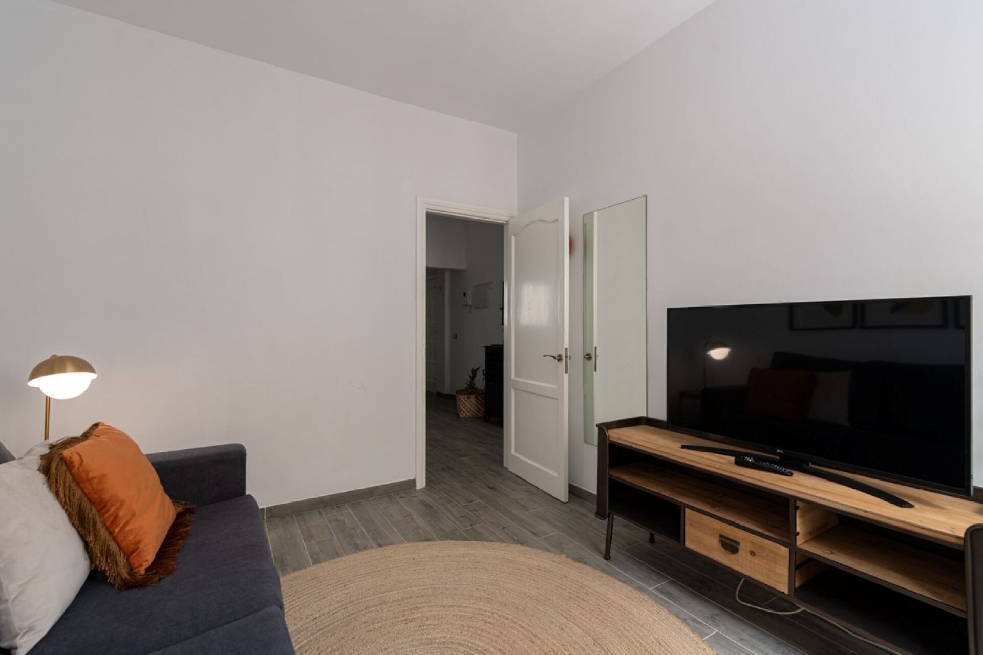 Un salon moderne avec un canapé de couleur sombre, un meuble de rangement en bois, un téléviseur à écran plat et une lampe.
