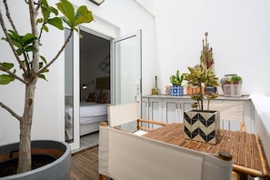 A room with a bed, a dining table, chairs, a potted plant, and a kitchen area with cabinets and a countertop.