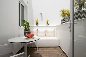 A small, white-walled room with a round table, a white sofa, and a potted plant.