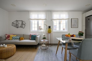 A modern living room with a sofa, a dining table, and a kitchen area.