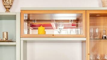 A flat-screen TV on a wooden cabinet with a glass shelf above it, containing a wine glass and a yellow object.