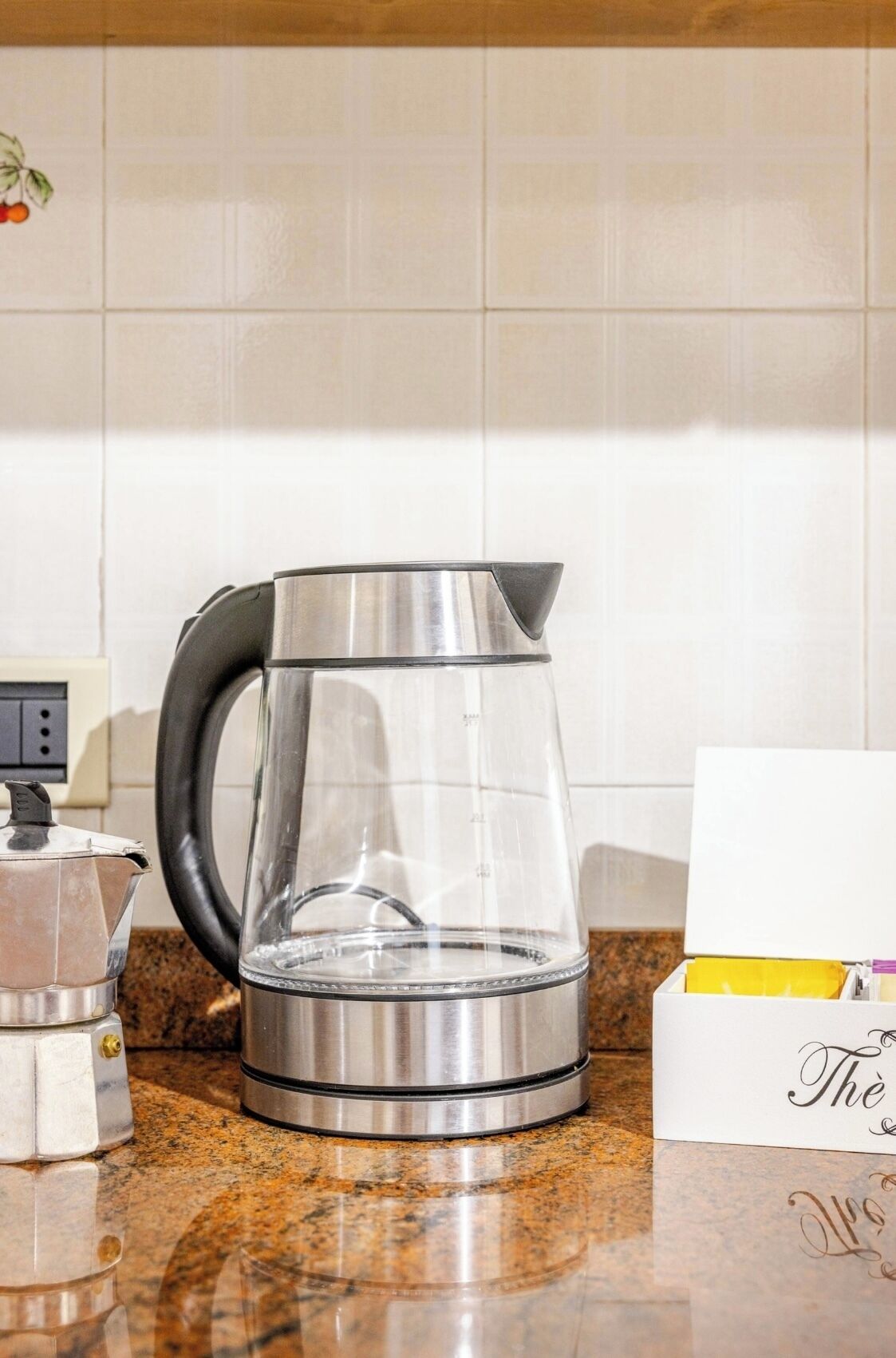 Ein Edelstahl-Wasserkocher auf einer Granit-Arbeitsplatte, eine weiße Karte mit handschriftlichem Text und eine kleine elektrische Kaffeemaschine.