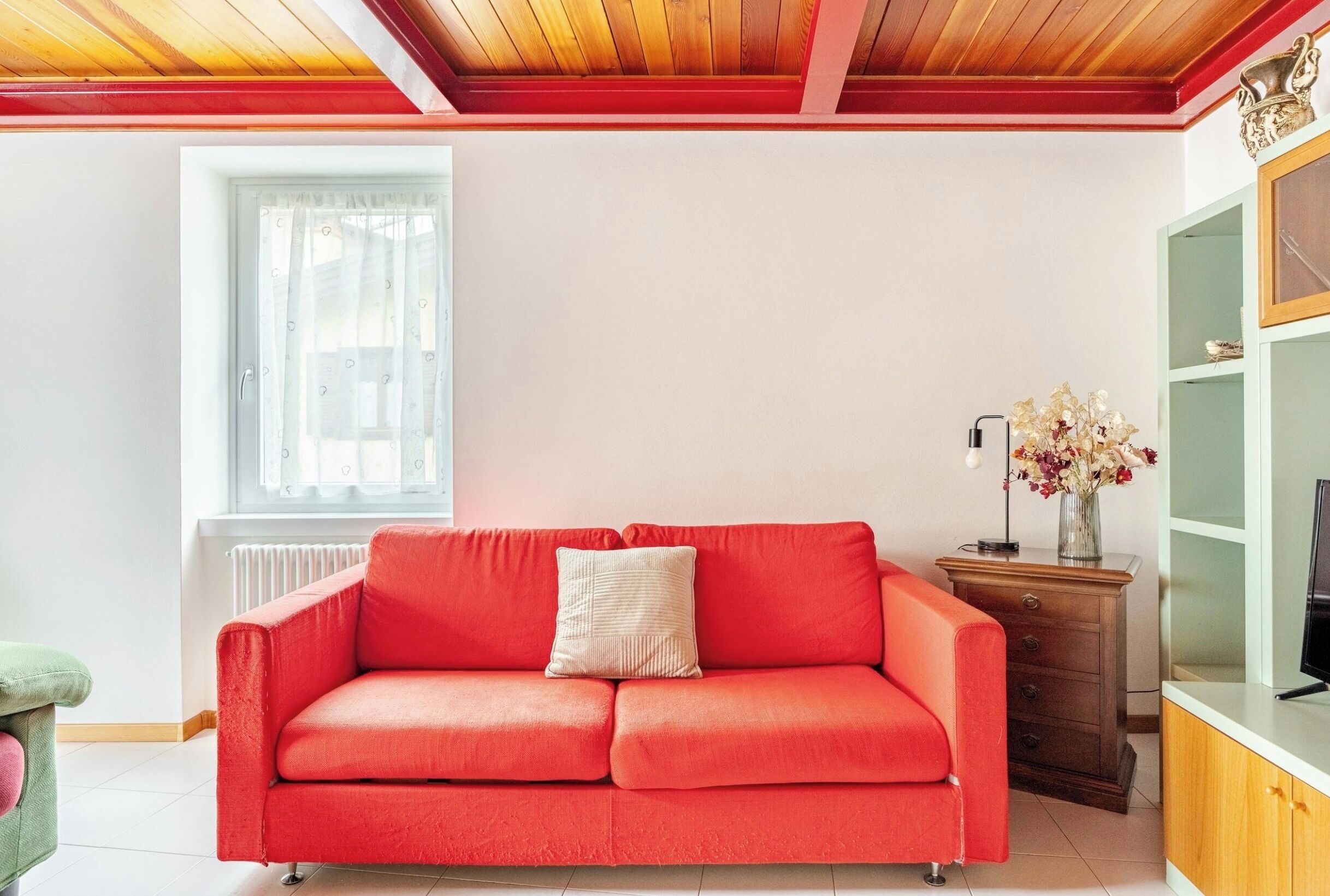 Un sofá rojo con un cojín, un mueble de madera y un jarrón con flores.