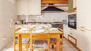 A modern kitchen with white cabinets, wooden ceiling beams, and a dining table set for four. - House at the Alley [near Lake Garda] (Vigo)