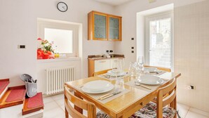 A dining area with a wooden table set for four, a kitchen with a window, and a radiator. - House at the Alley [near Lake Garda] (Vigo)