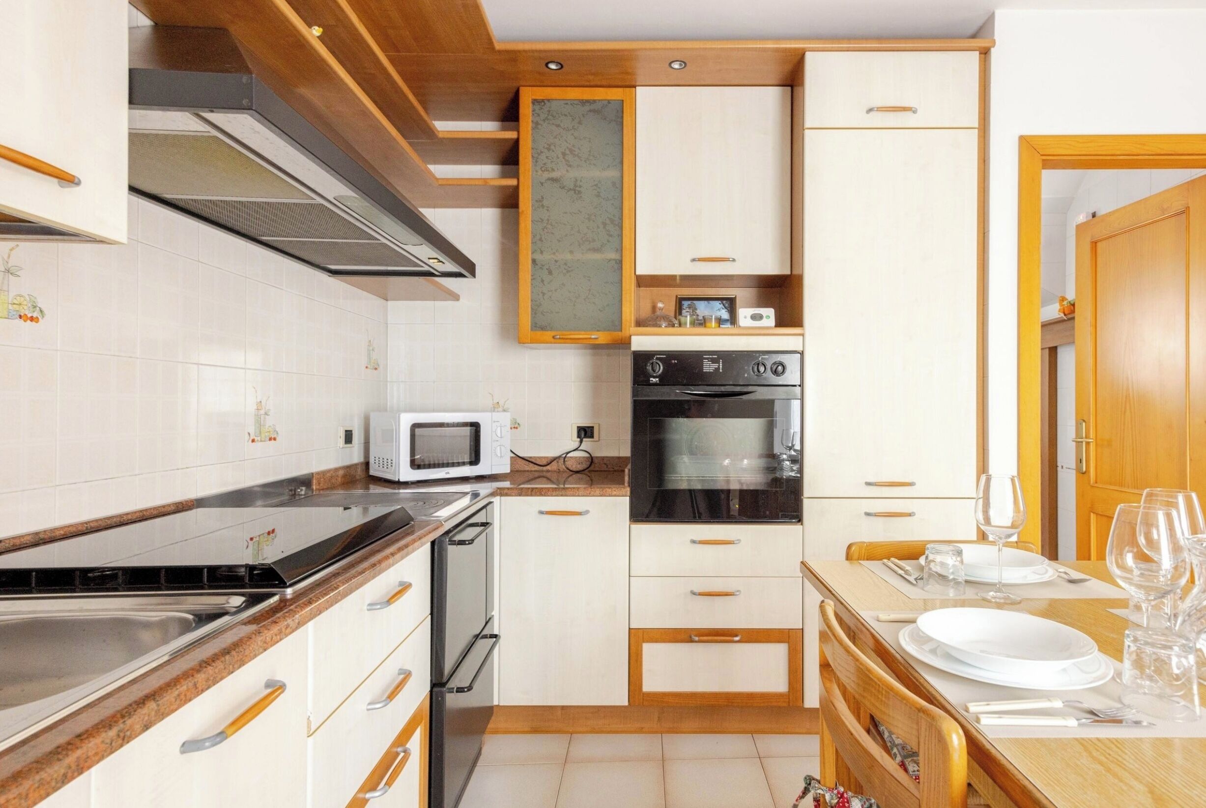 Een kleine keuken met witte kasten, een magnetron, een oven en een houten aanrecht.