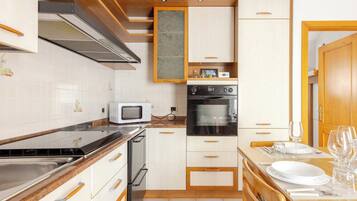 Een kleine keuken met witte kasten, een magnetron, een oven en een houten aanrecht.