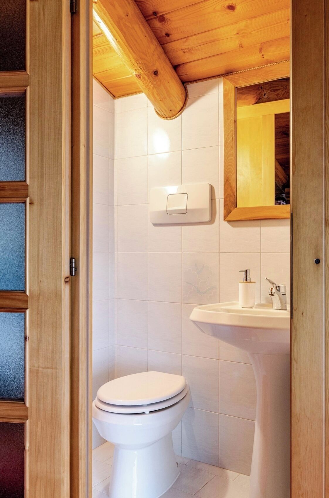 Un baño con inodoro blanco, techo de madera y lavamanos blanco con espejo superior.