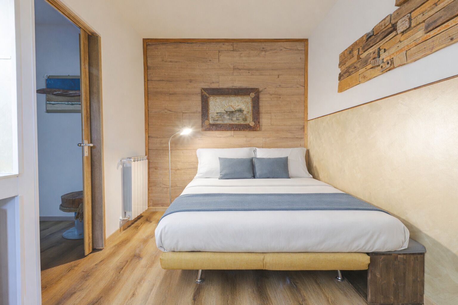A bedroom with a wooden headboard, a bed with white bedding and blue pillows, a radiator, and a framed picture on the wall.