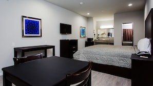 Habitación de hotel con cama, escritorio, silla, televisión y baño visible a través de una puerta abierta.