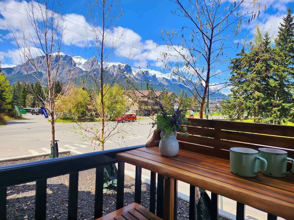 A wooden bench with a vase and two mugs, overlooking a road with cars and a mountain backdrop.