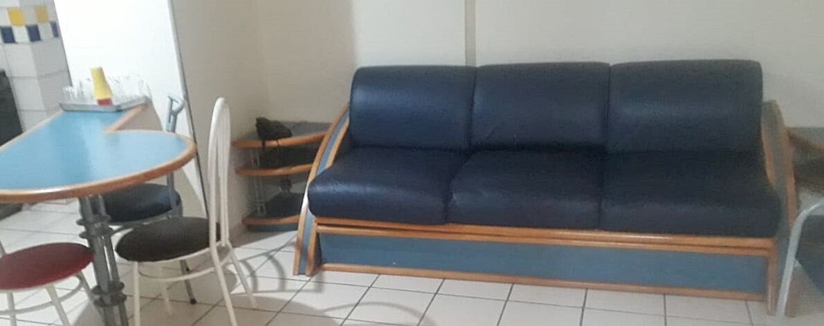 Un sofá azul y una pequeña mesa redonda con sillas en una habitación con suelo de baldosas.