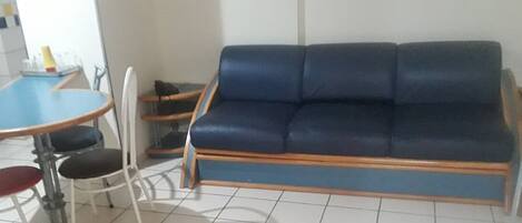 Un sofá azul y una pequeña mesa redonda con sillas en una habitación con suelo de baldosas.