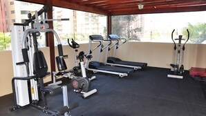 Un gimnasio al aire libre techado con diversos equipos de ejercicio, incluyendo cintas de correr, una máquina de pesas y una bicicleta estática.