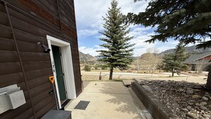 A wooden building with a green door, a concrete pathway, and a stone retaining wall.