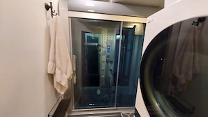 A compact bathroom with a glass shower enclosure, a towel rack, and a small shelf.