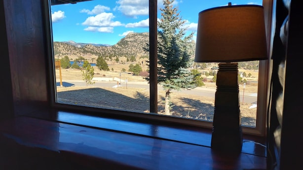 A window with a view of a mountainous landscape, a lamp on the windowsill, and a wooden floor.