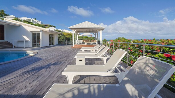 Une terrasse en bois avec des chaises longues, une piscine et un kiosque.