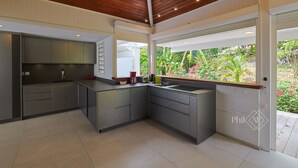 Une cuisine moderne avec des meubles gris, un plafond en bois et une vue sur un jardin grâce à de grandes fenêtres.