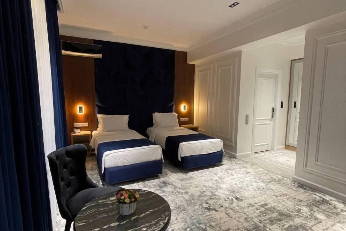 Une chambre d’hôtel avec deux lits, une table ronde ornée d’un vase de fleurs et un sol à motifs de marbre.