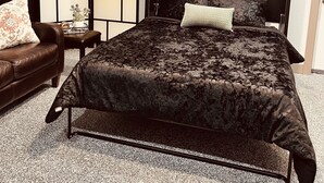 Een slaapkamer met een groot bed, een kleintje tafeltje met een plant, een leren bank en een wandairconditioner.