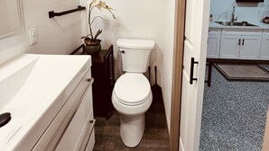 Een compacte badkamer met een wit toilet, een klein wastafeltje en een orchidee in pot.