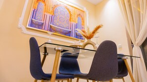 Un comedor con una mesa de vidrio, dos sillas azules y un adorno en la pared.