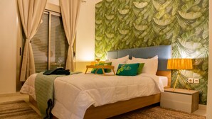 Un dormitorio con cama, mesitas de noche, lámpara y pared decorada con un diseño de hojas.