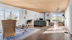 A spacious living room with a large window, a fireplace, and a view of the outdoors. - Cozy home in Sydals with sauna (Sydals)