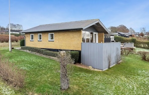Une maison de plain-pied avec une façade en briques, un toit gris et une cour arrière clôturée.