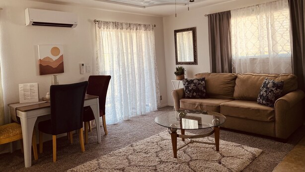 Un salon comprenant une table basse en verre, un canapé, un ventilateur de plafond et un coin repas avec des chaises et une table.