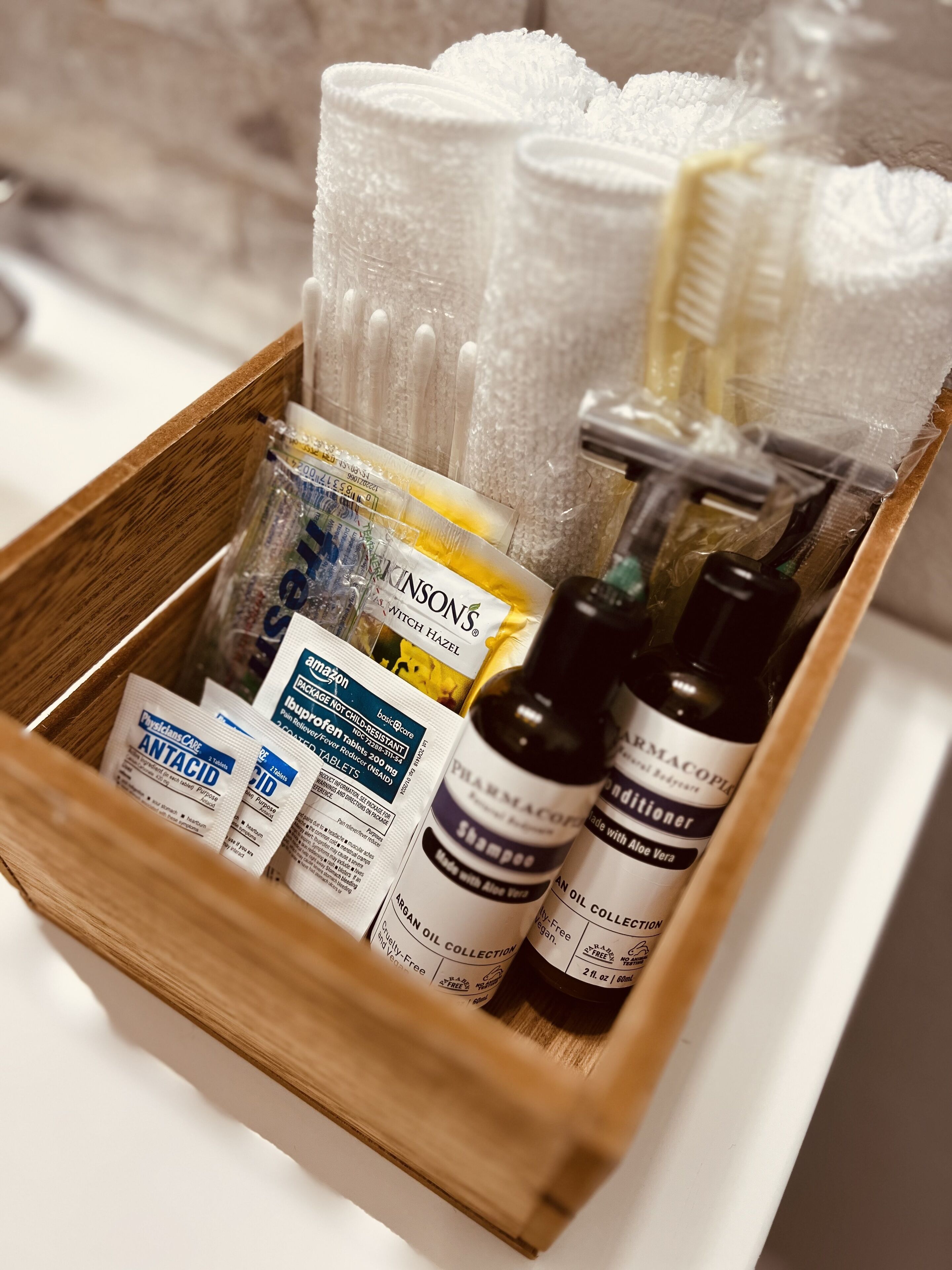 A wooden tray containing toiletries including a bottle of shampoo, a bottle of conditioner, and several packages of oral care products.