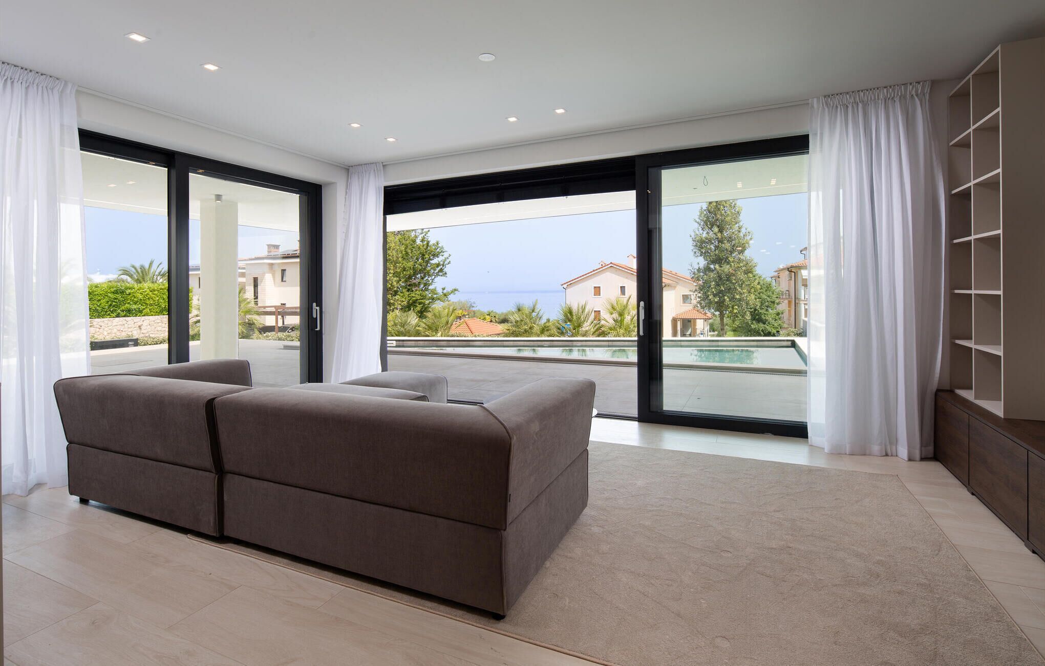 Un dormitorio moderno con una cama grande, puertas de vidrio correderas a un balcón y vistas al mar y edificios.