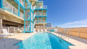 A swimming pool with a clear blue water, surrounded by a white fence and a building with blue railings.