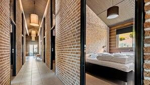 Een moderne hotelgang met zichtbare bakstenen muren, een centrale doorgang en een slaapkamer met een bed en raam.