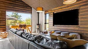 Een moderne woonkamer met een leren bank, een grote flatscreen-tv en een houten plafond.