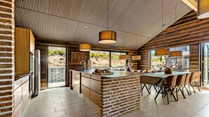 Een moderne keuken met een keukeneiland van baksteen, roestvrijstalen apparatuur en een groot raam met uitzicht op een natuurlandschap.