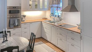 Une cuisine moderne avec des armoires blanches, un plan de travail en bois, un four encastré et une fenêtre avec des rideaux.