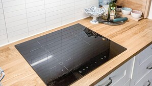 Une cuisine dotée d’une plaque de cuisson à induction noire, d’un plan de travail en bois et d’un dosseret carrelé blanc.